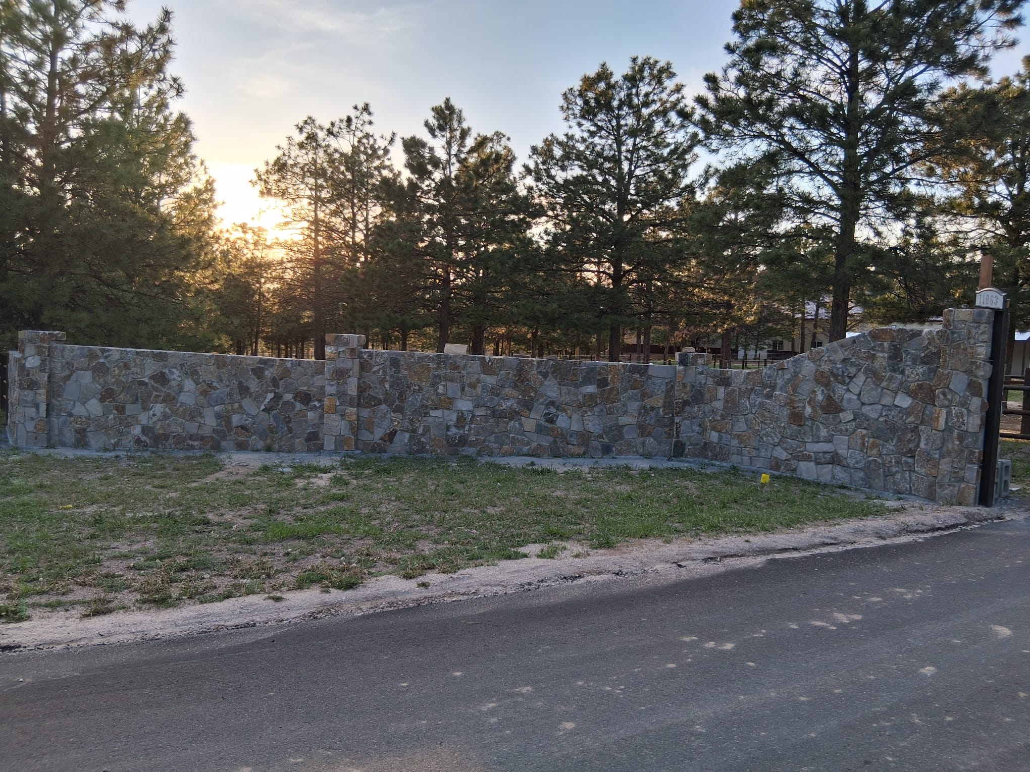 A rustic stone entrance wall with an integrated mailbox pillar and house number.